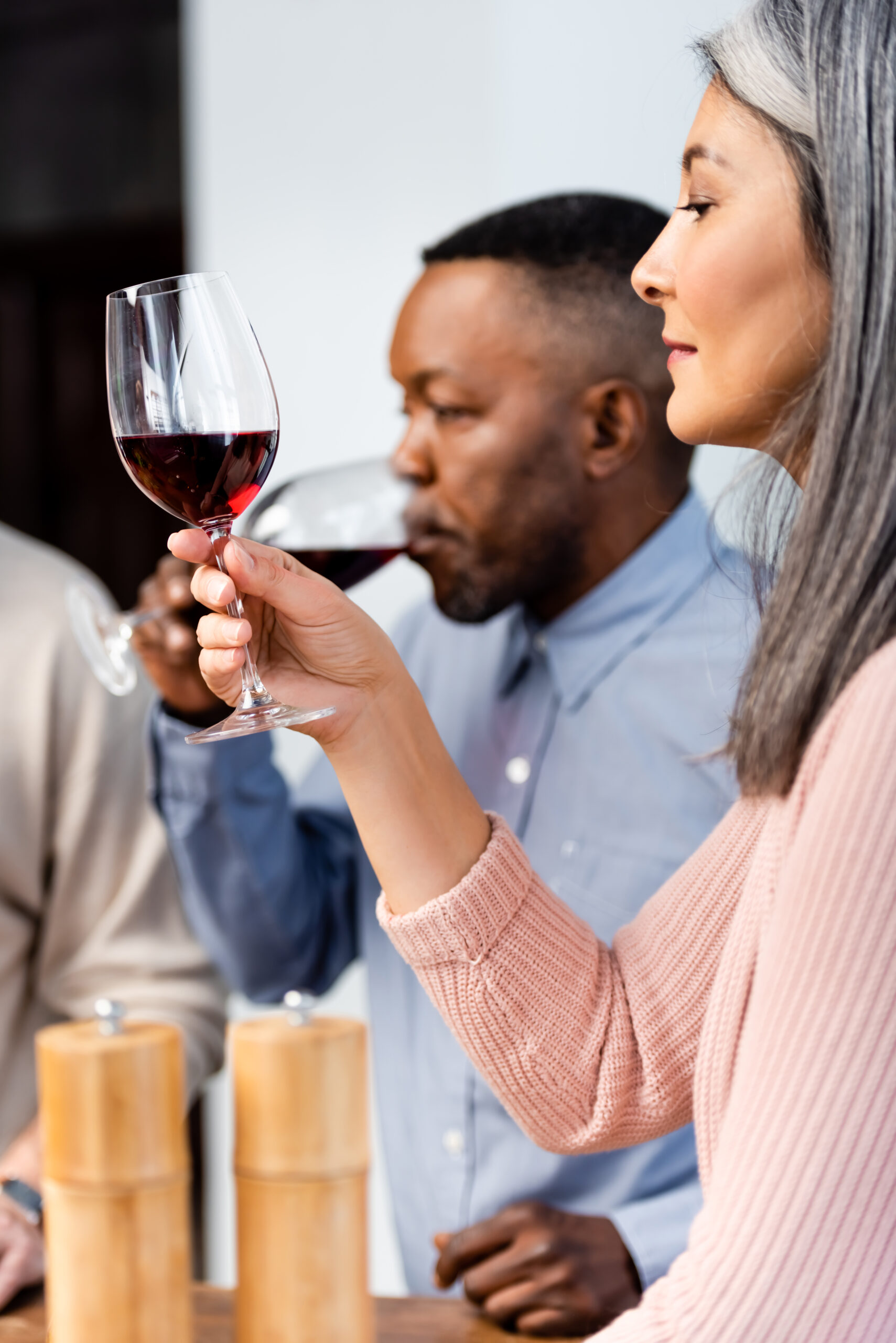 selective focus of asian woman looking at wine glass and african american man drinking wine